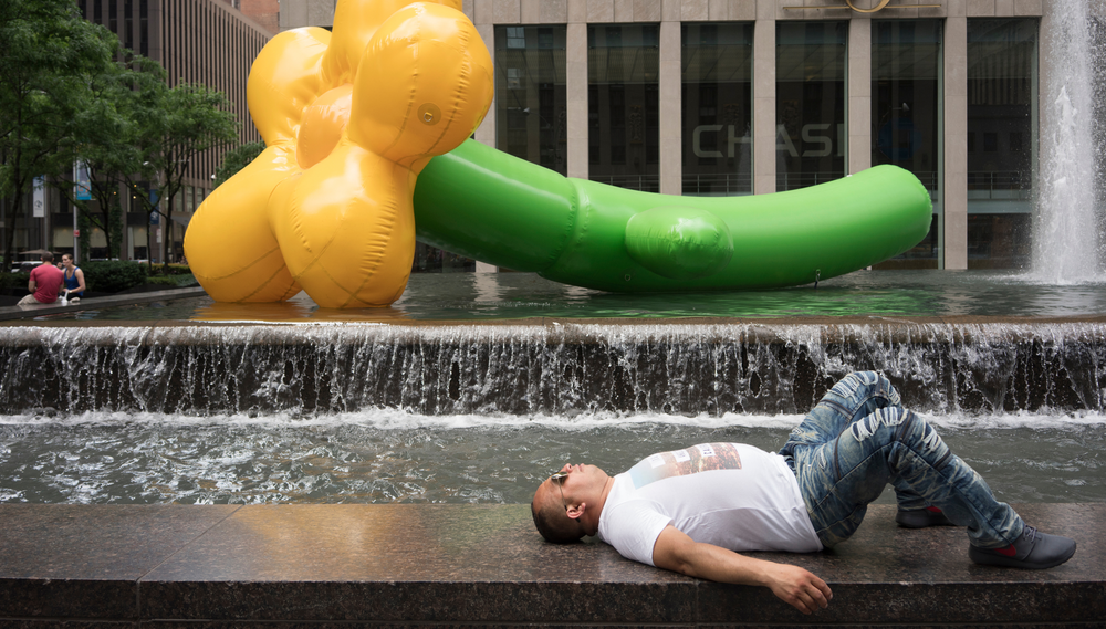 A man lies on a fountain ledge beneath large inflatable sculptures