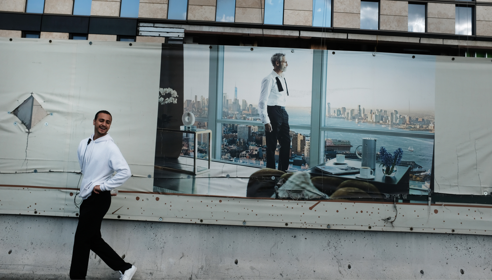 A man walks in front of an advertisement for a luxury apartment building that depicts a man in a suit with his tie undone looking out the floor-to-ceiling window at the city skyline