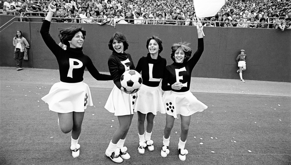 Four cheerleaders, each one wearing a sweater with one letter of Pelé's name, cheer for the soccer player on the field during his last game for the New York Cosmos.