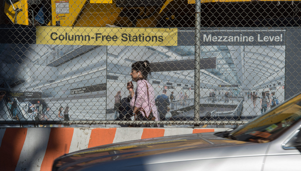 A woman walks in front of construction site displaying a sign advertising the Second Avenue Subway station that is being built there