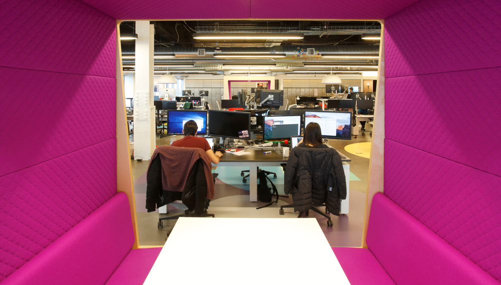 A view of an office seen through the pink walls of a cubicle