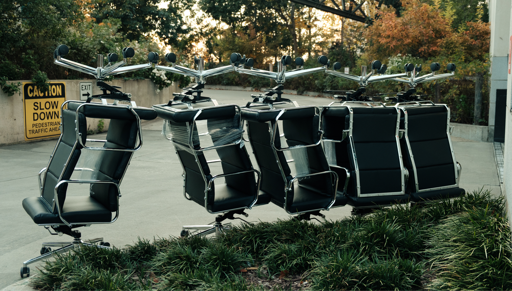 Several office chairs sit outside an office building, with some stacked upside down on top of others