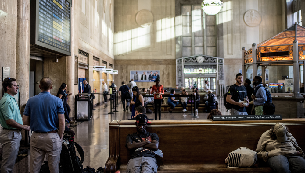 People sit on benches and others stand near benches at Newark, NJ's Penn Station