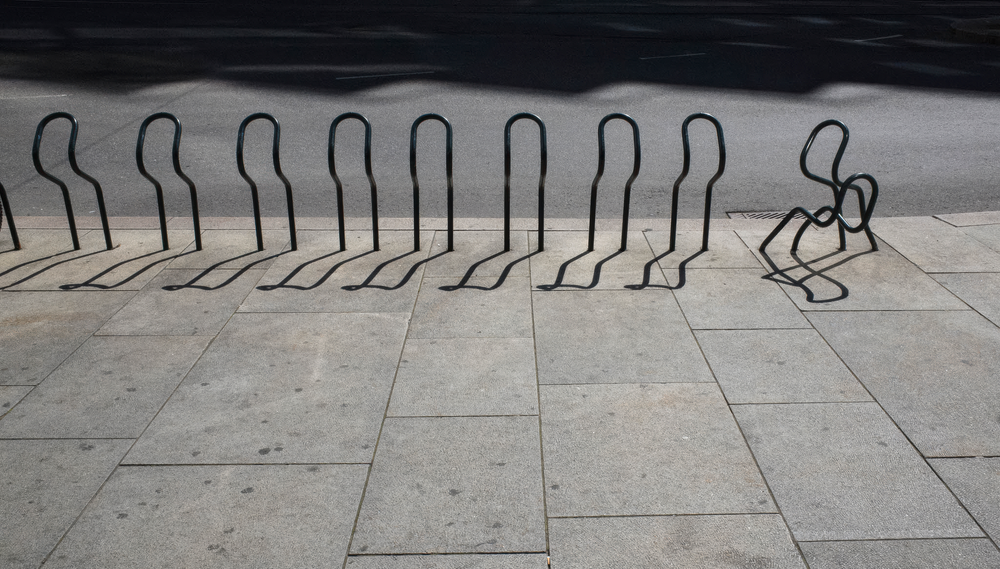 A row of bike racks on a city sidewalk, the rightmost rack twisted out of shape