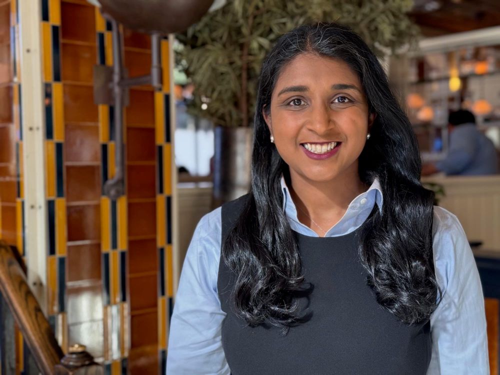 Saritha Komatireddy in a light blue shirt and dark vest beside a tiled wall in a restaurant