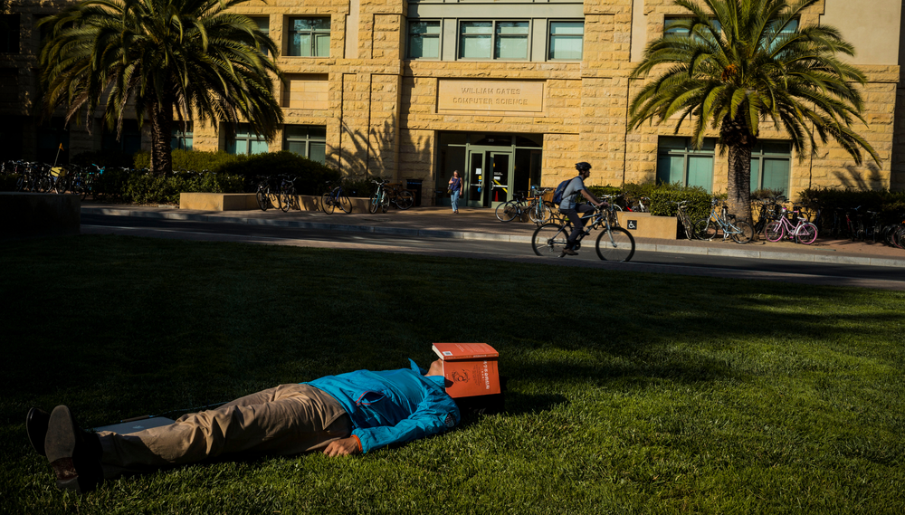 Person lies on a lawn with a red book over their face