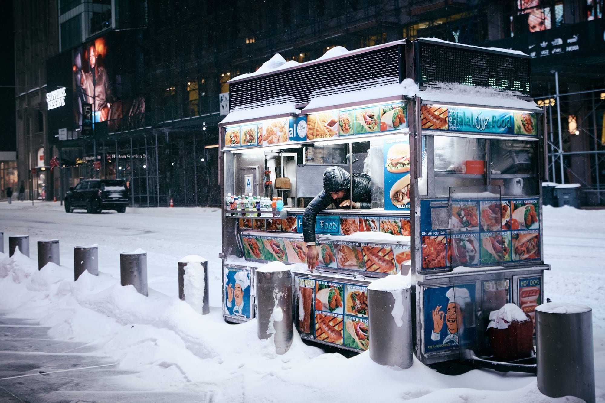 A Halal cart vendor reaches out of his cart during a snowstorm