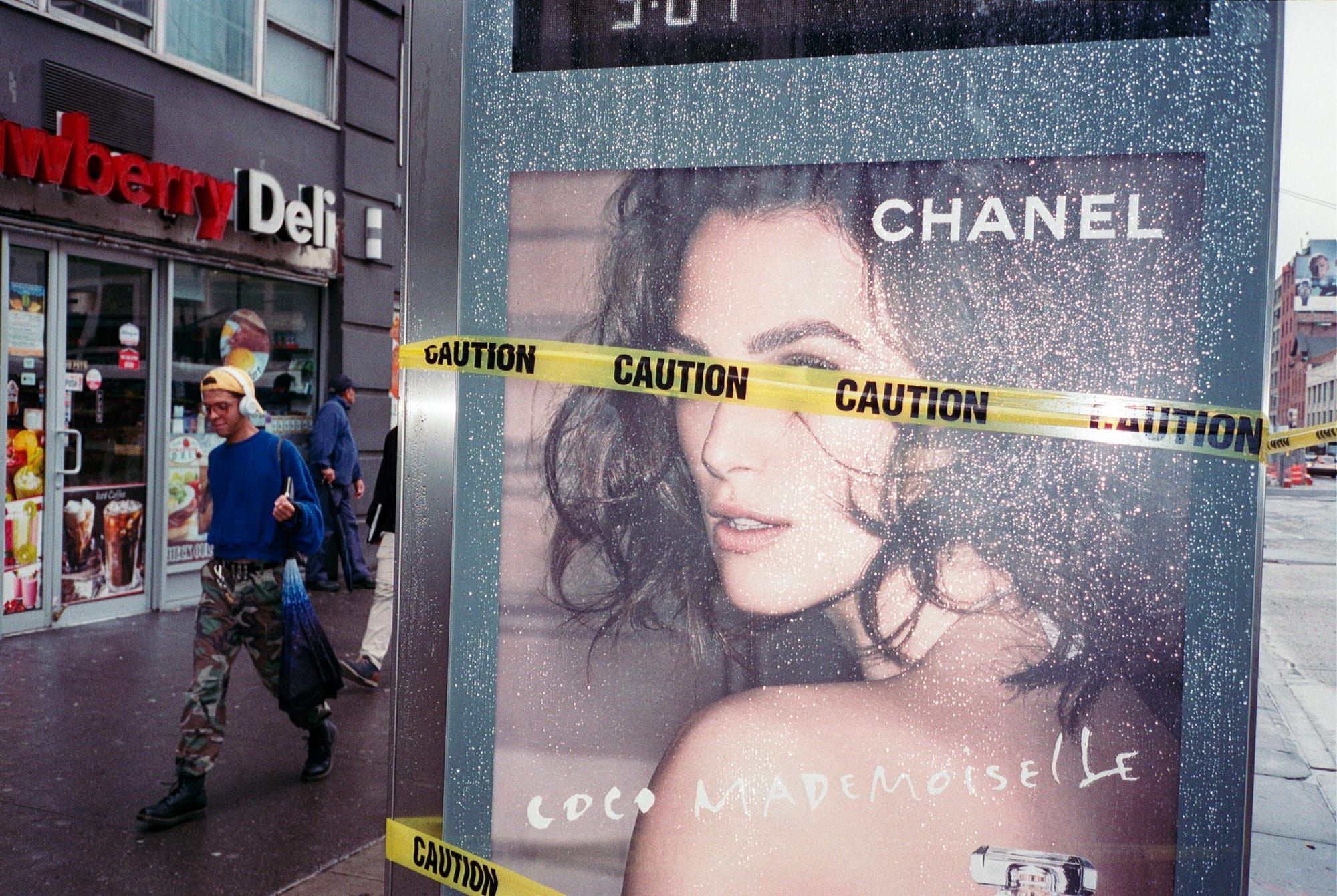 A man walks by a bus stop displaying a Chanel ad with caution tape wrapped across it
