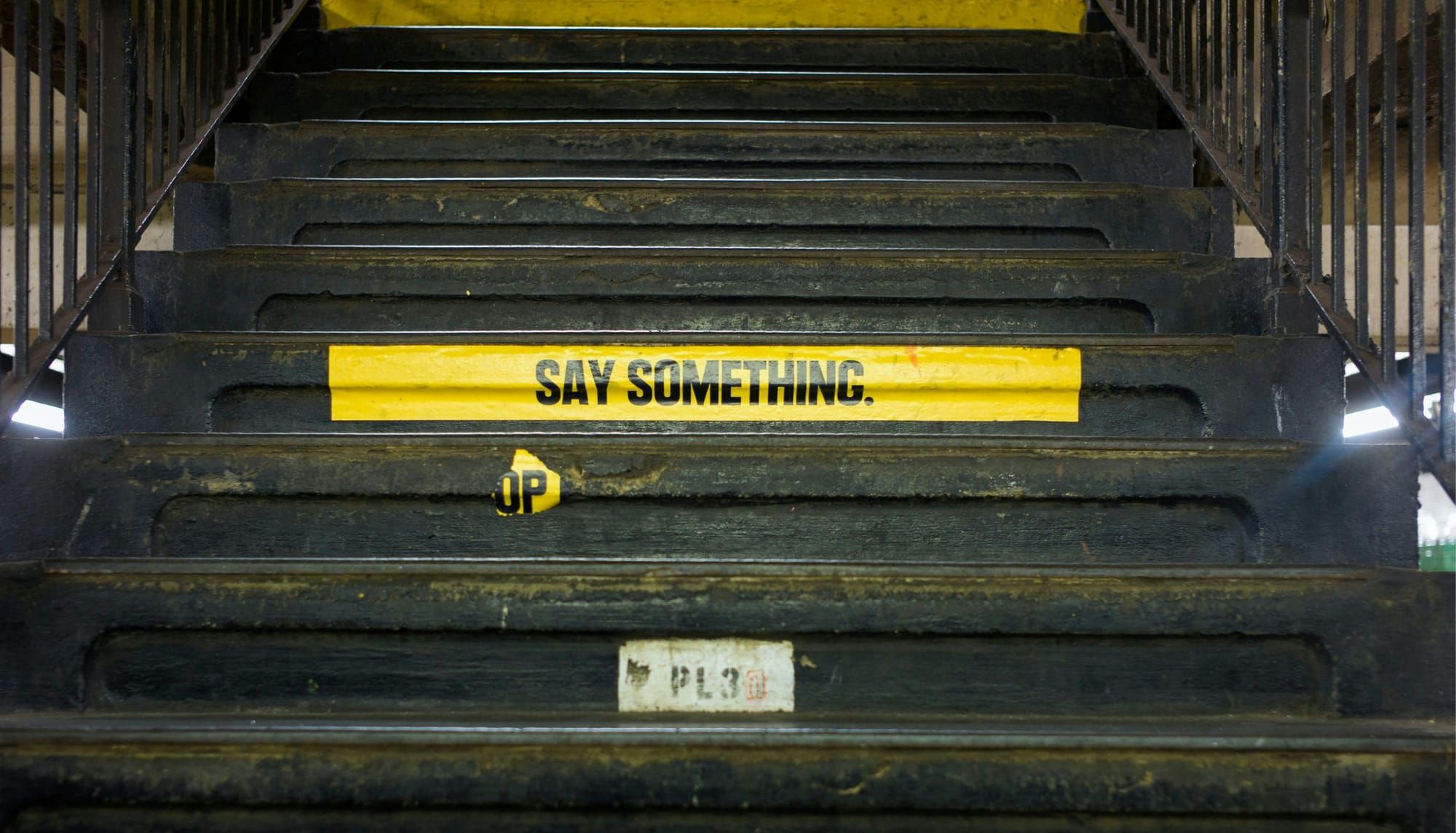 Dark subway stairs with yellow sign that reads "SAY SOMETHING"