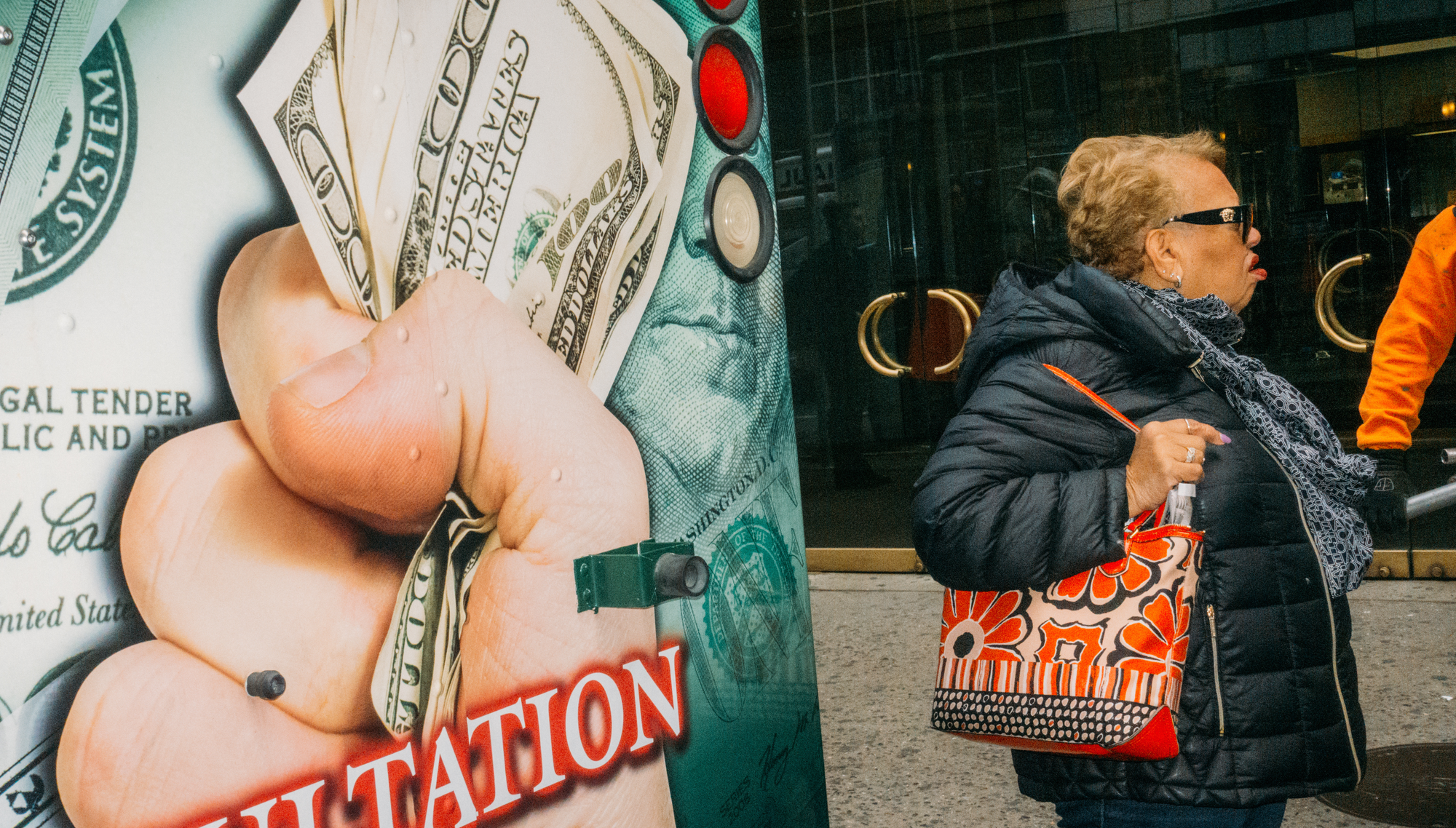 A woman stands to the right of a wall displaying an image of a hand holding several $100 USD bills