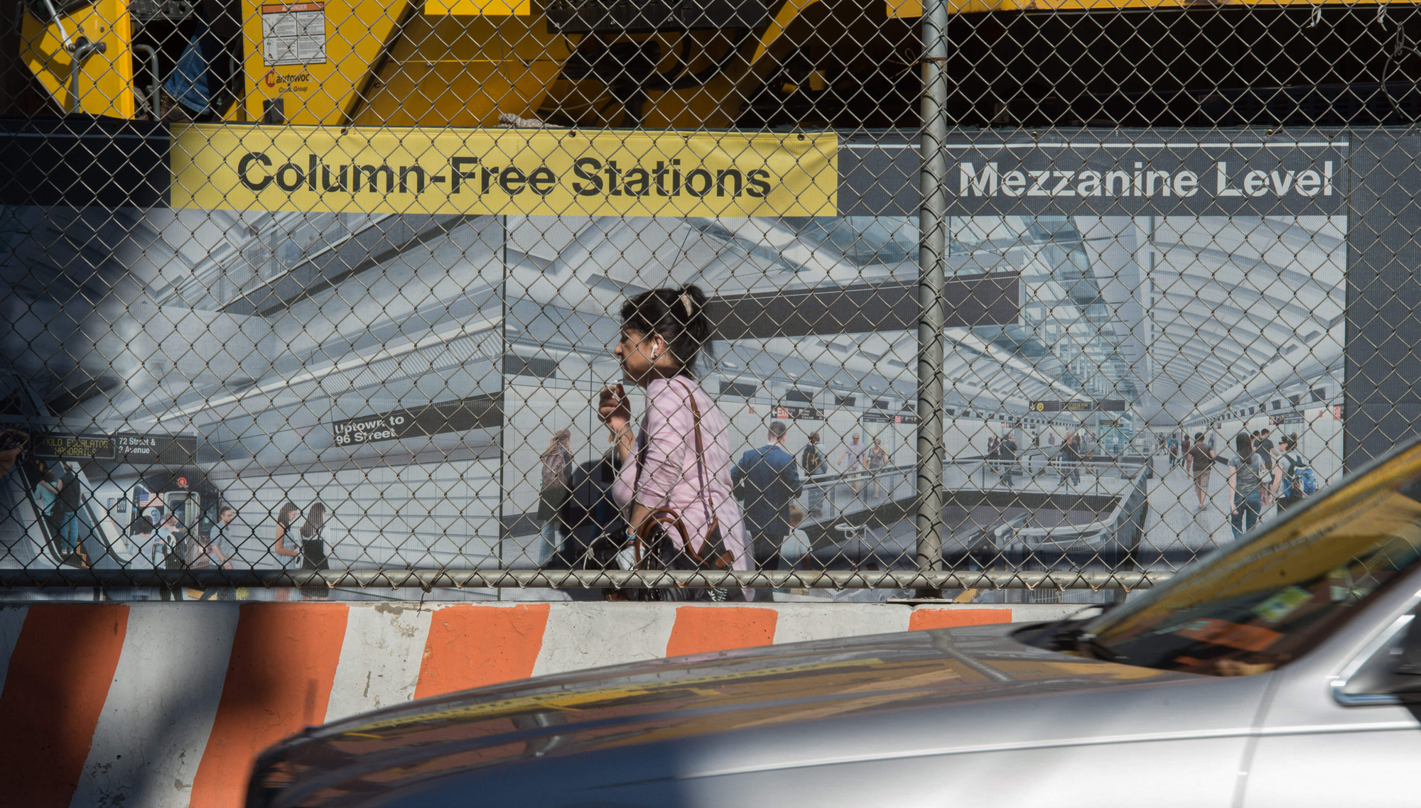 A woman walks in front of construction site displaying a sign advertising the Second Avenue Subway station that is being built there
