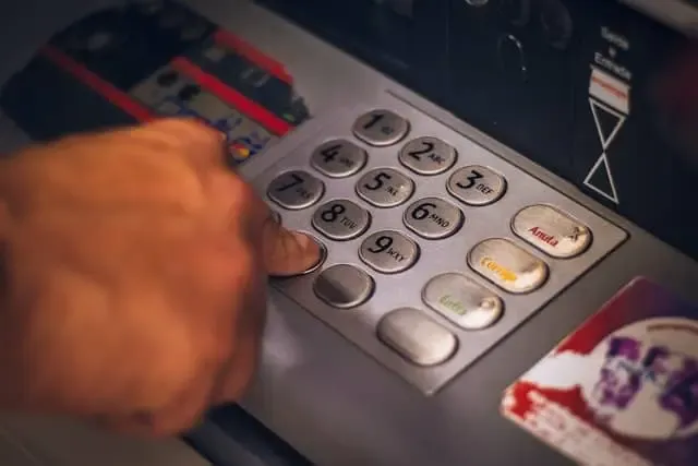 A hand pressing numbers on an ATM keypad, representing easier access and traditional banking integration for regulated stablecoins.