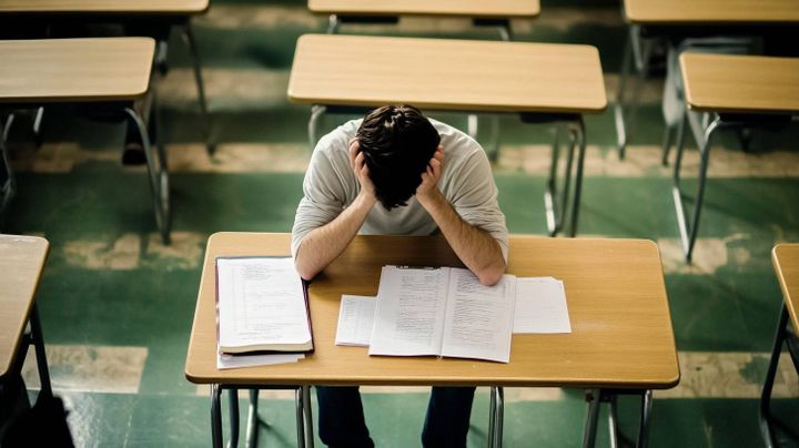 Image of a student in an exam hall holding their head in their hands