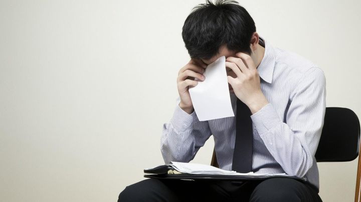 Image of a male student in a suit and tie with his head in his hands