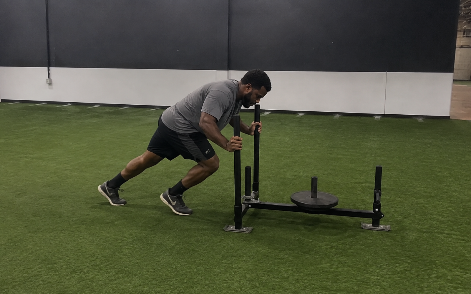 Athlete moving from a run into a weighted sled push during hybrid fitness training.