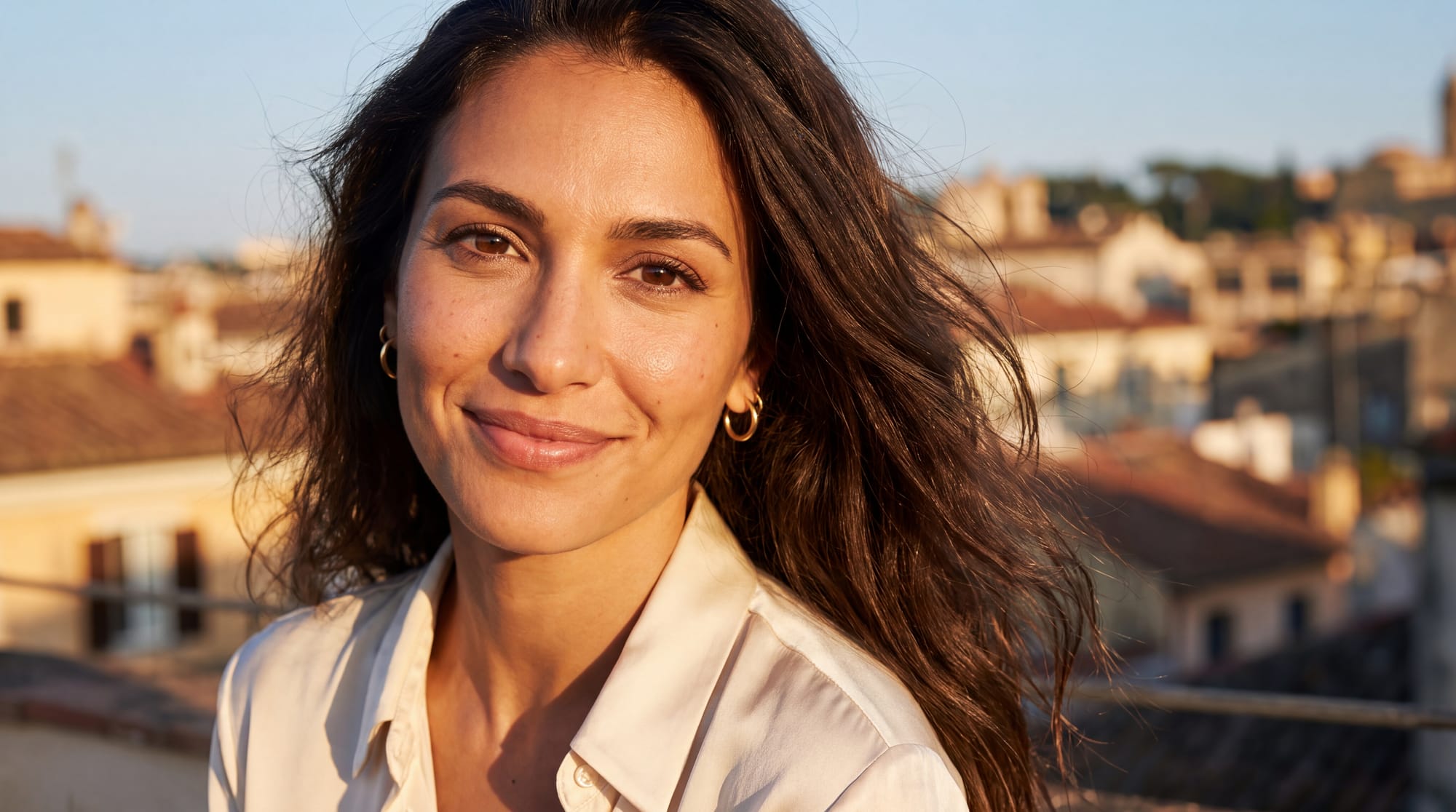 Close portrait of a beautiful 25-year-old Mediterranean woman standing on a bright rooftop terrace at golden hour.