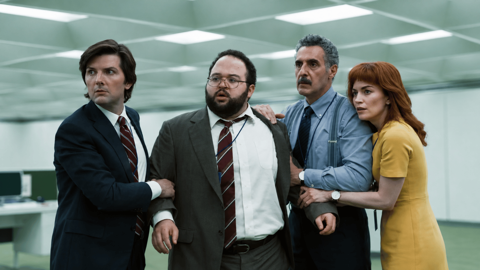 Four uneasy office workers stand together inside the sterile green-and-white Lumon workplace.