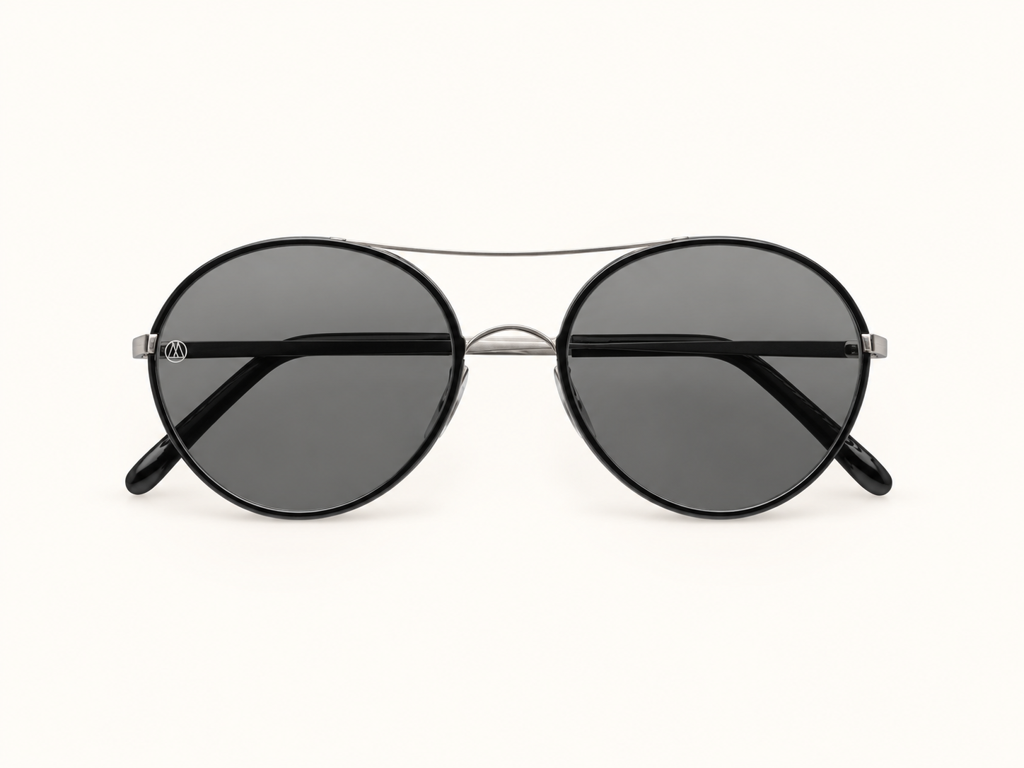 Round black sunglasses with grey lenses and a slim silver double bridge, shown front-on against a warm ivory background.