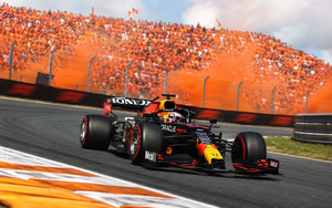 Max Verstappen's Red Bull racing through a banked corner at Zandvoort in front of packed orange grandstands.