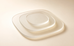 Three translucent frosted-glass rounded panels, decreasing in size and stacked with visible gaps, sit against a warm ivory gradient background with soft studio lighting and subtle shadows.