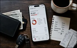 Rocket Money's budgeting dashboard displayed on a smartphone beside a wallet, receipts and handwritten budget notes.