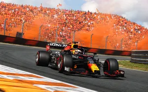Max Verstappen's Red Bull racing through a banked corner at Zandvoort in front of packed orange grandstands.