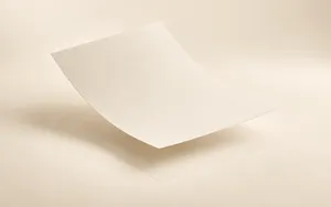 A single sheet of cream paper lifting slightly off a warm ivory surface as if floating upward