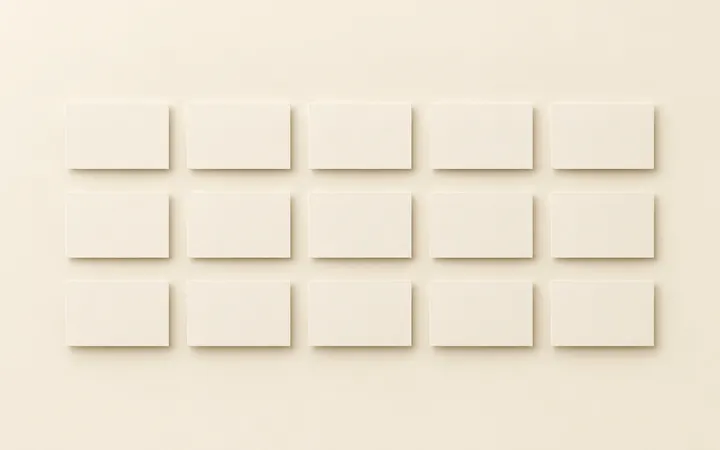 A clean grid of small identical blank rectangular cards, evenly spaced and evenly lit on a seamless warm ivory surface