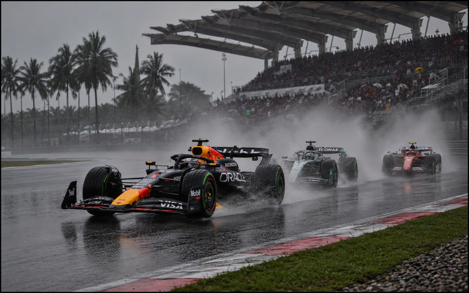 Three Formula 1 cars racing through heavy spray at Malaysia’s Sepang International Circuit.