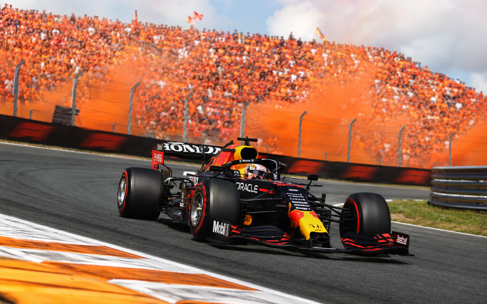 Max Verstappen's Red Bull racing through a banked corner at Zandvoort in front of packed orange grandstands.