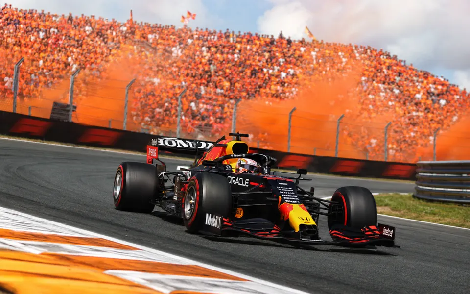 Max Verstappen's Red Bull racing through a banked corner at Zandvoort in front of packed orange grandstands.