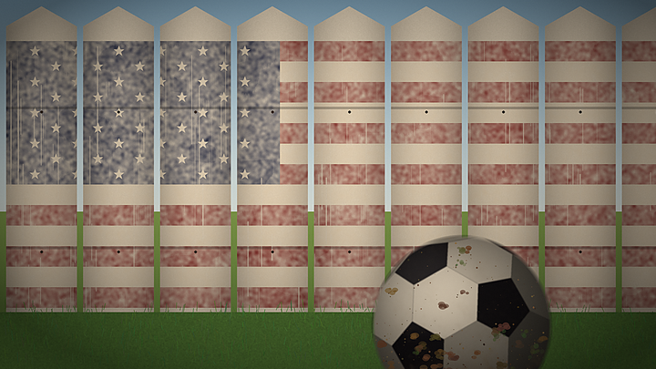 Dirty soccer ball in front of a faded American flag paited on a wooden picket fence.