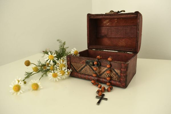 flowers next to a small wooden box with a beaded necklace coming out of it, with a cross