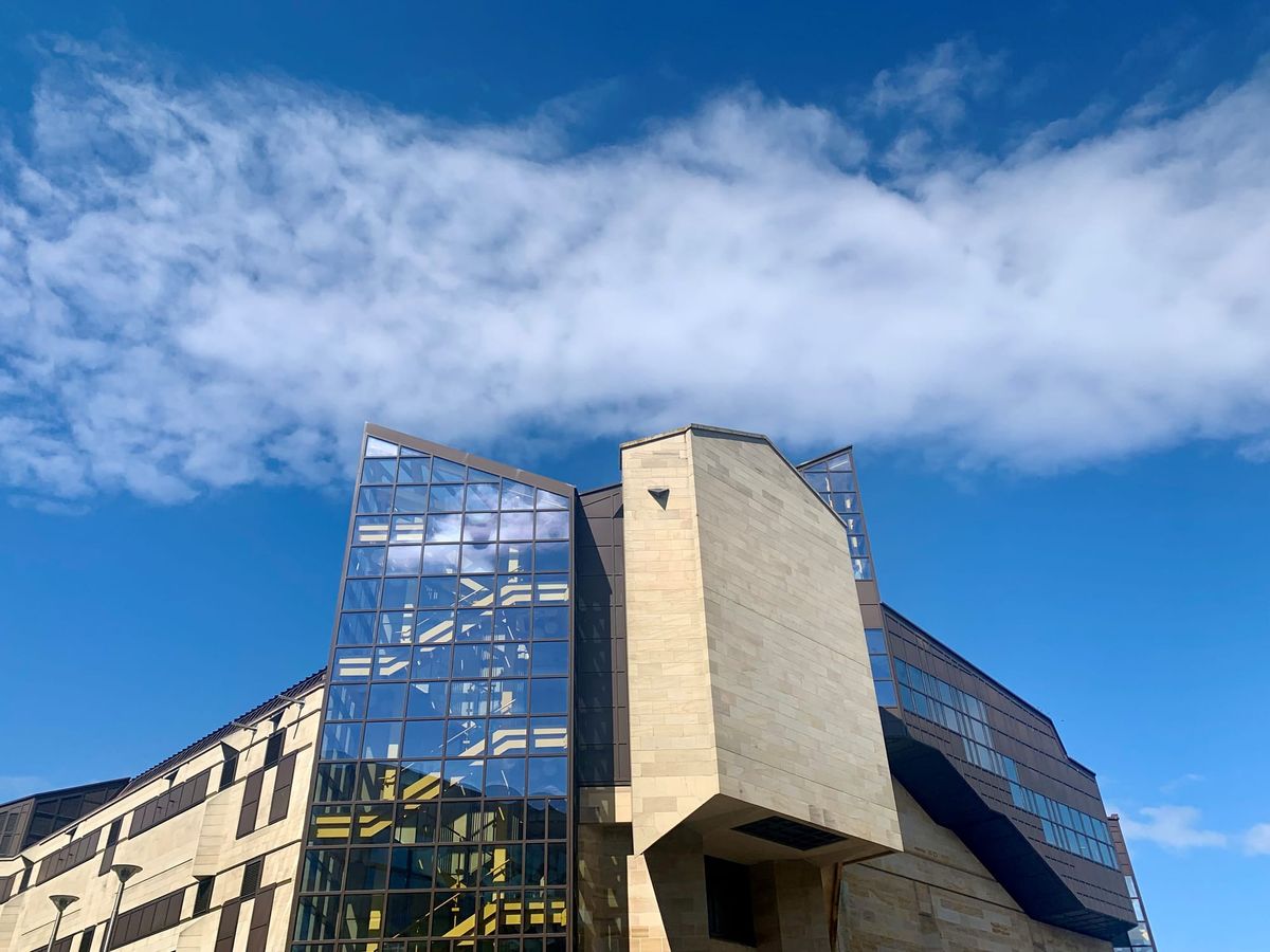 Stone and glass building in front of a blue sky with white cloud.