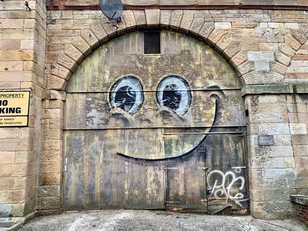 Smiley face graffiti on on wooden door in a large stone archway.