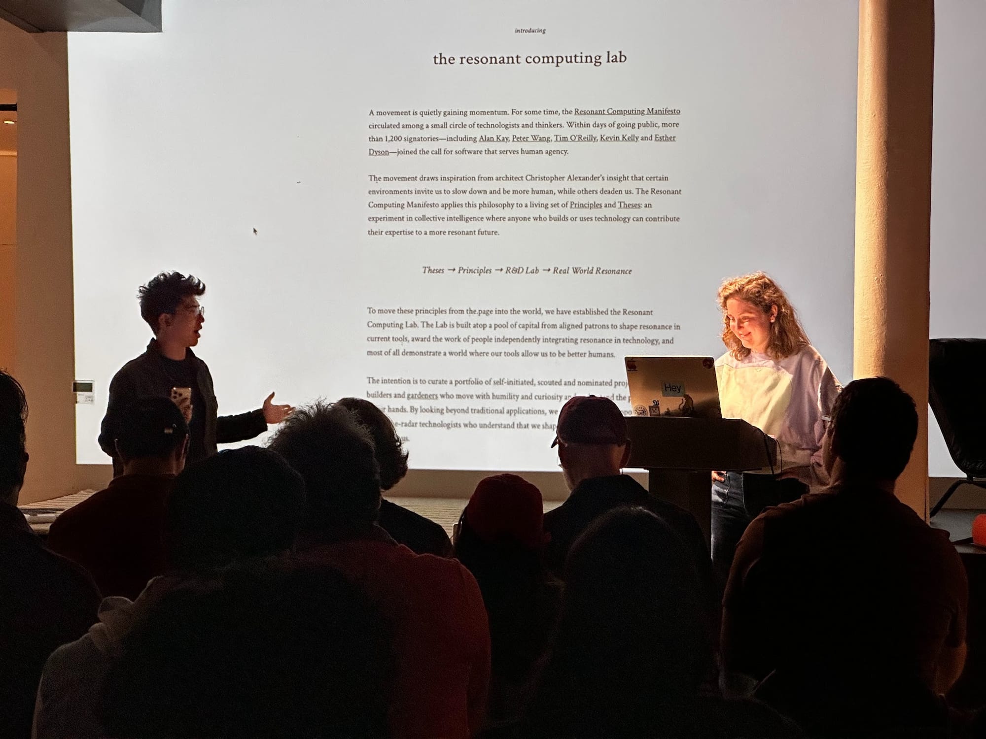 Two presenters introduce the Resonant Computing Lab to a seated audience, standing in front of a large projected slide titled "introducing the resonant computing lab.