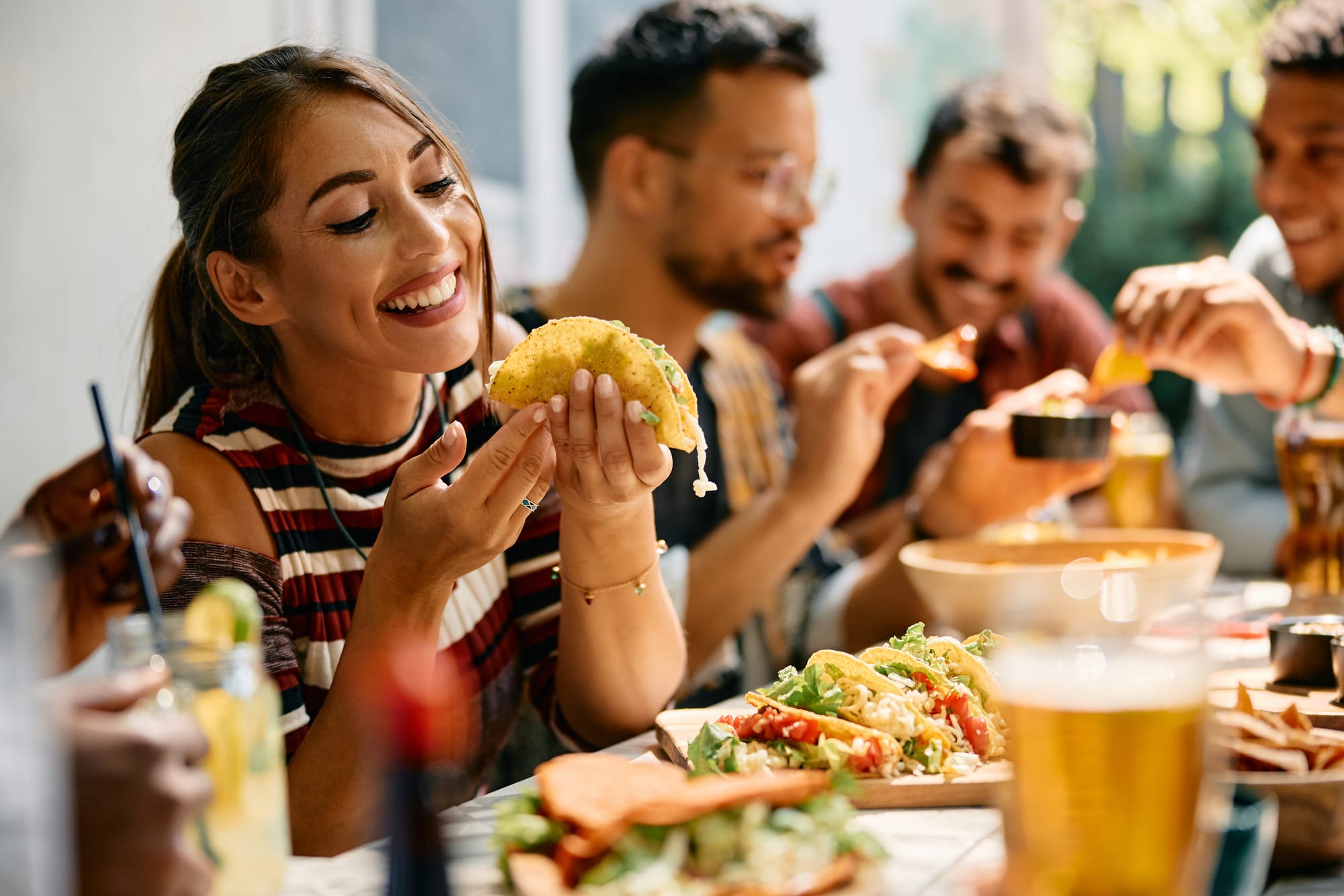 Woman enjoying al pastor tacos alongside carnitas and other types of tacos.