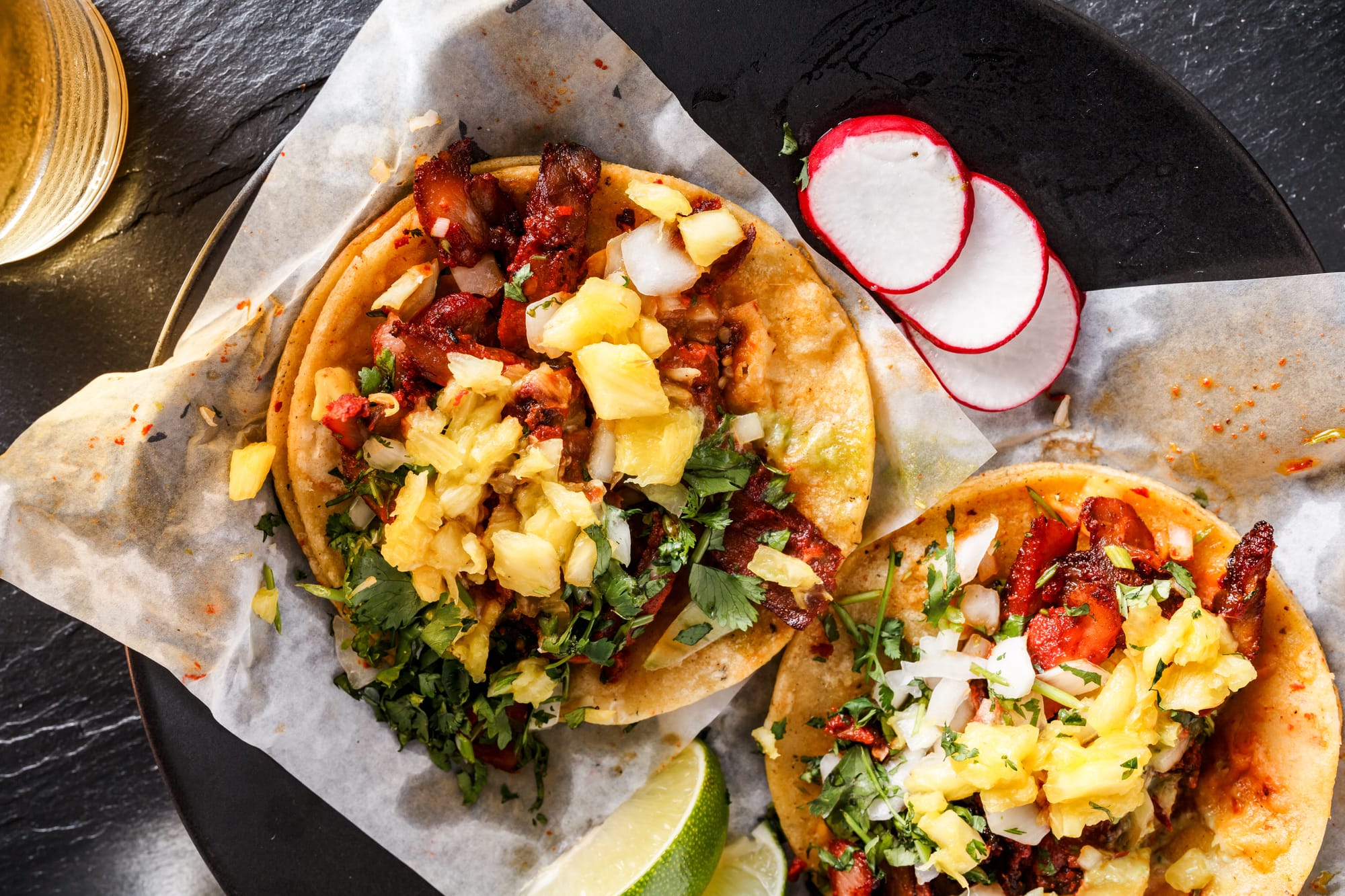 Tacos al pastor with pineapple chunks and salsa verde.