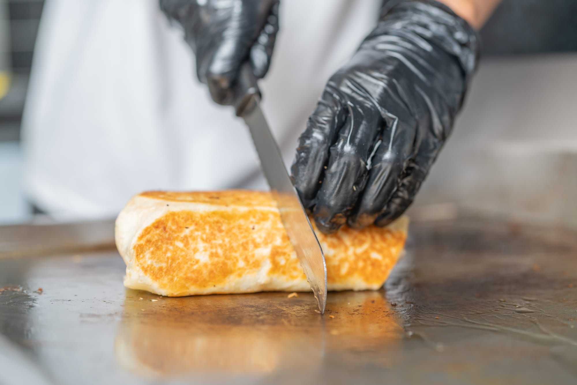 Mexican chef cutting an al pastor burrito in half.