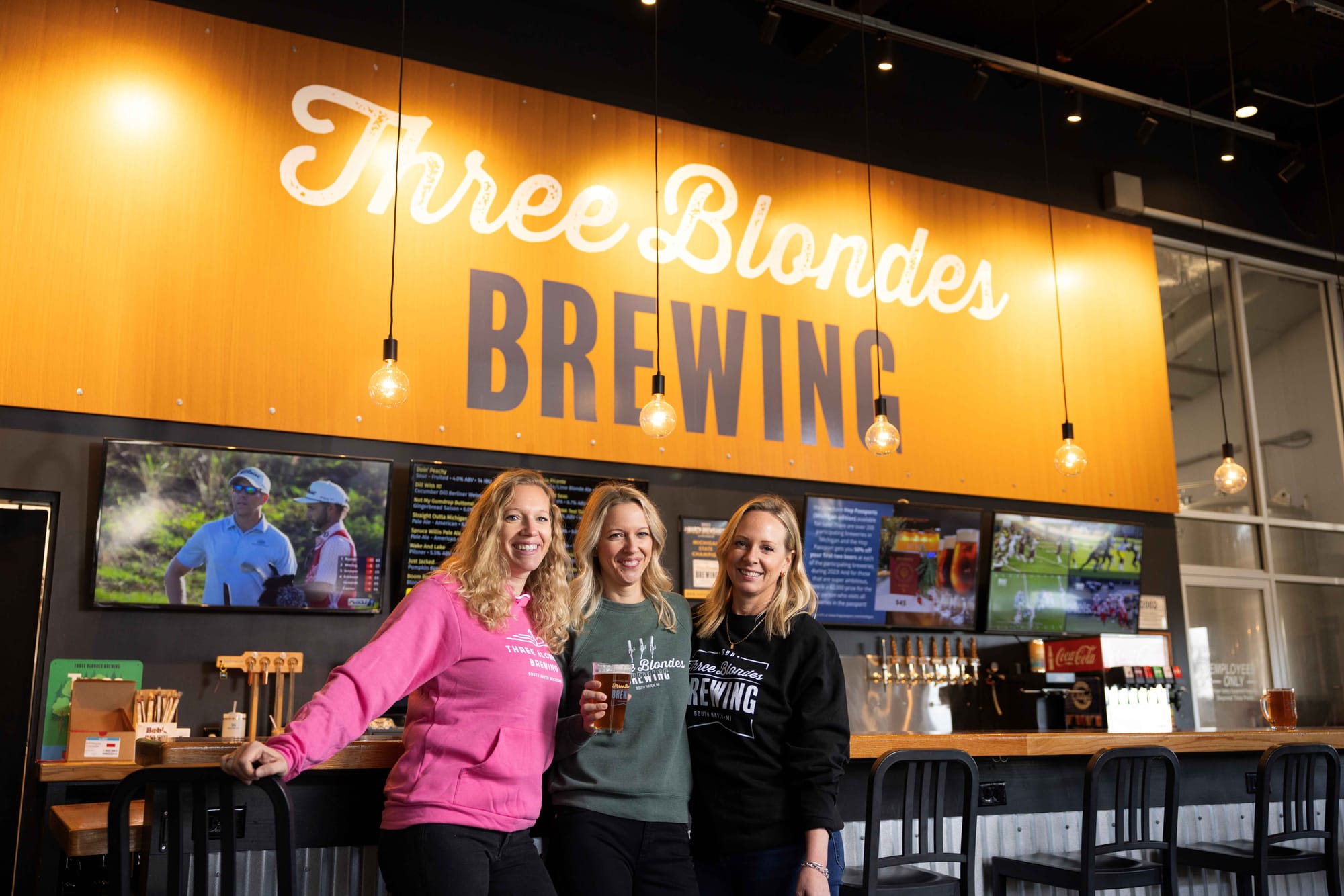 The three sisters and co-owners of Three Blondes Brewing standing in front of the bar