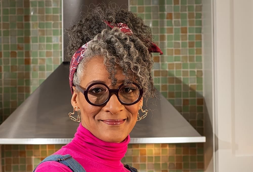 Carla Hall in at her cooking studio in a pink turtleneck.