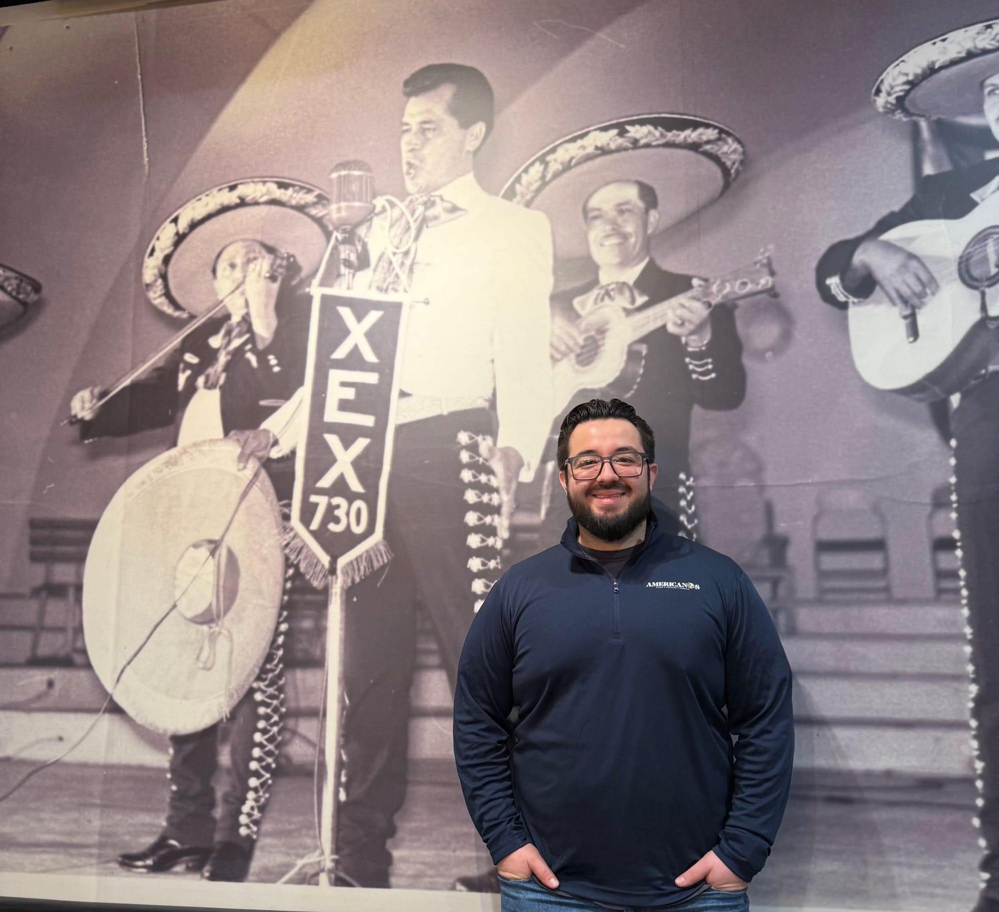 AJ Castillo at Americanos restaurant in Chicago, standing in front of a poster of his grandfather, Alfonso, who was mariachi singer