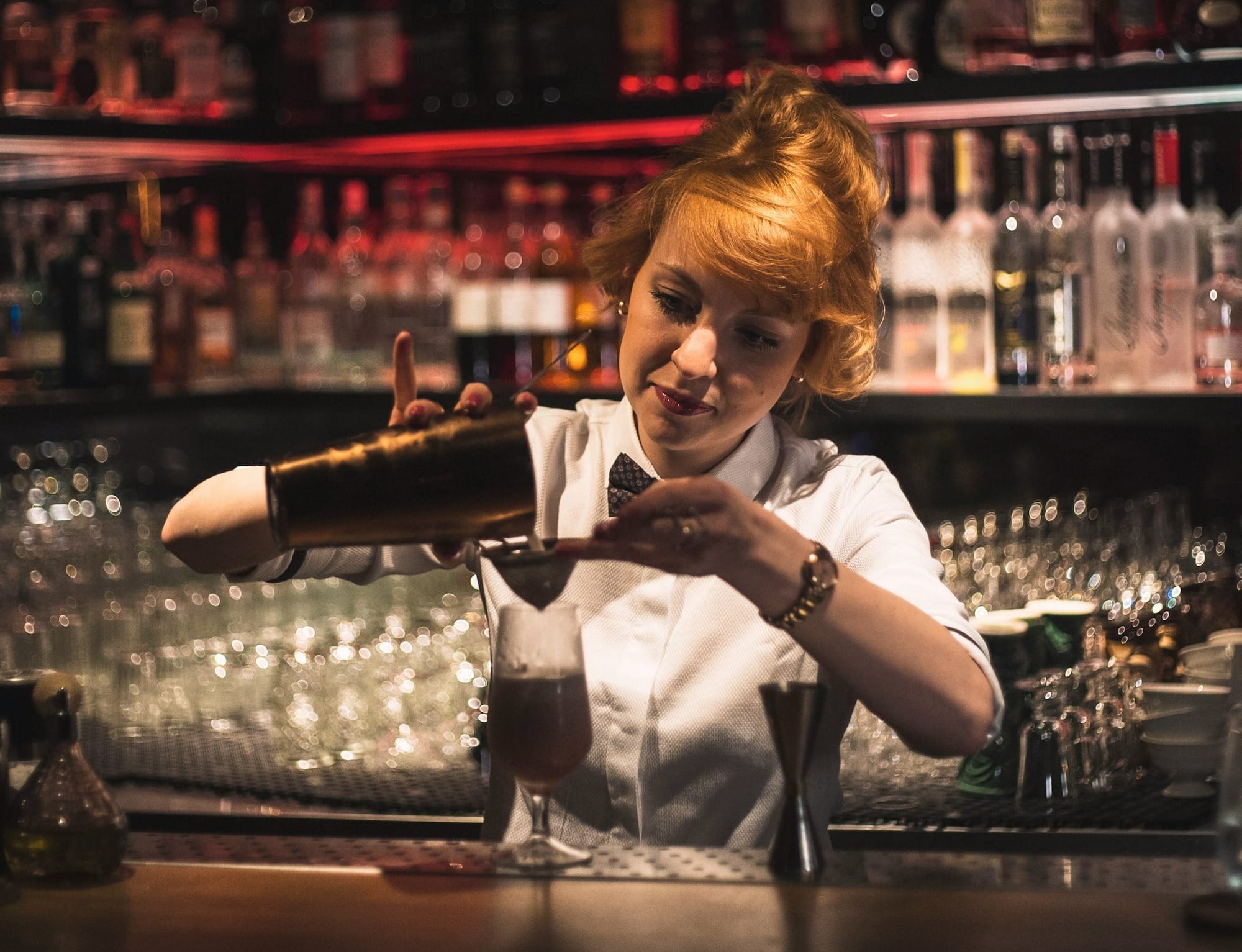 Woman behind bar pouring bar shaker in clear glass stem glass on bar counter