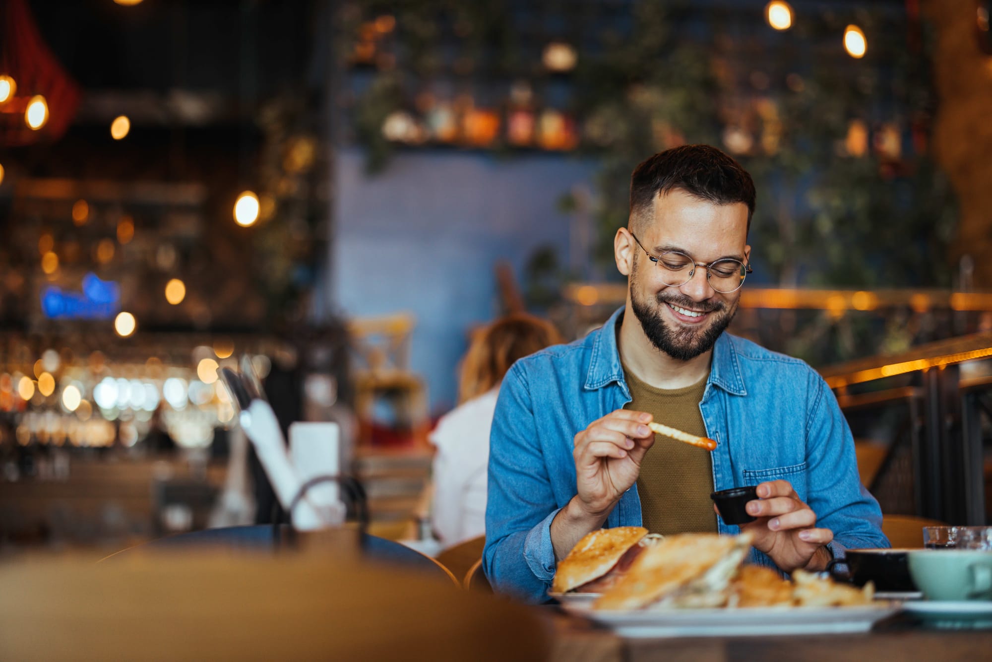 Man seated in a restaurant smiling while holding a french fry