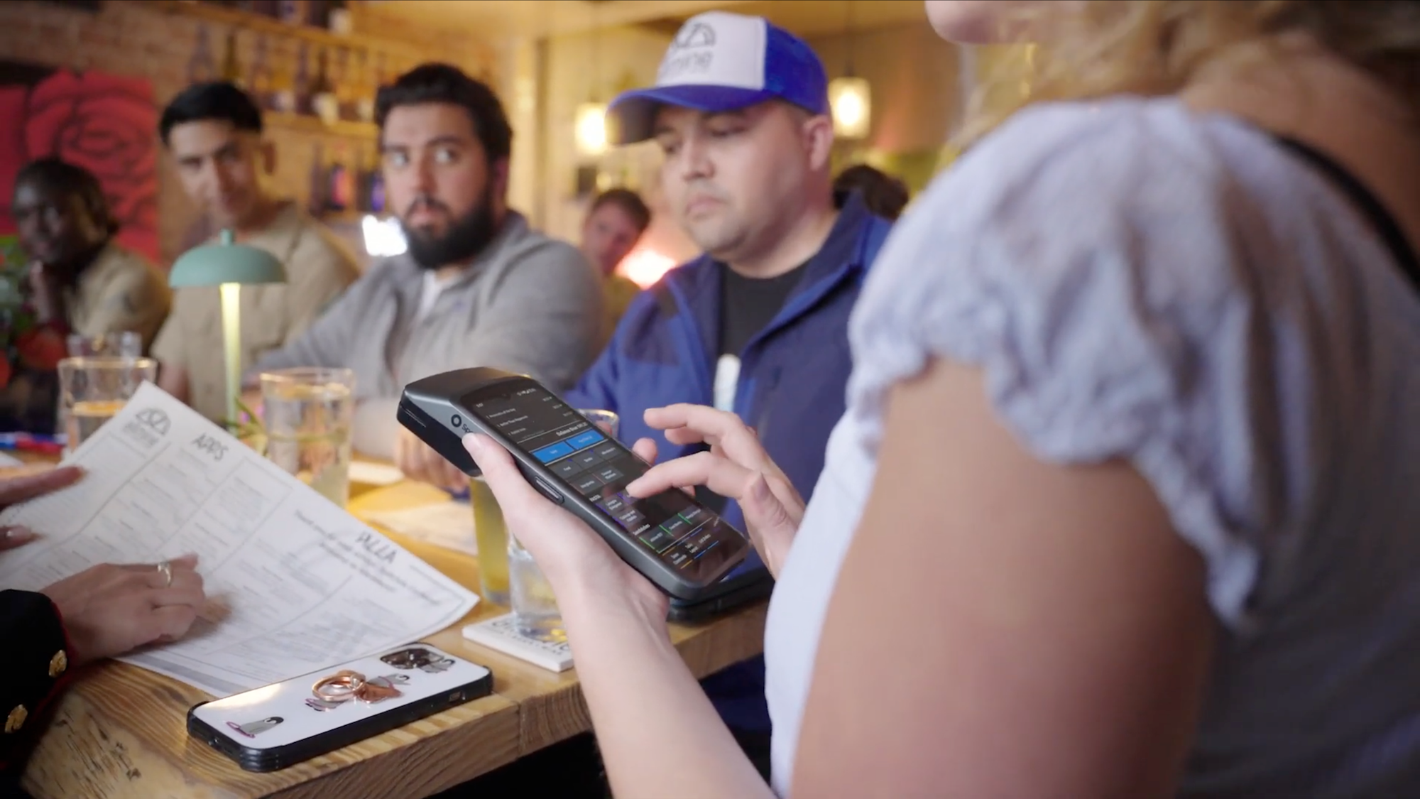 Server with a handheld at a table of guests.
