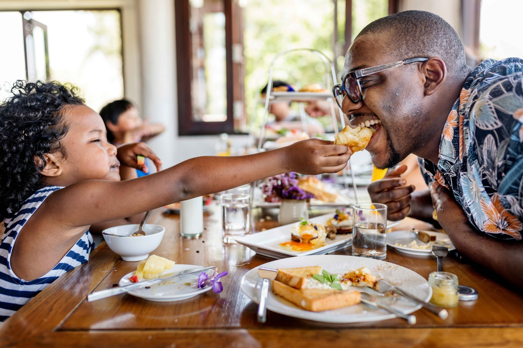 A little girl gives her dad a bite of food from her plate at a restaurant