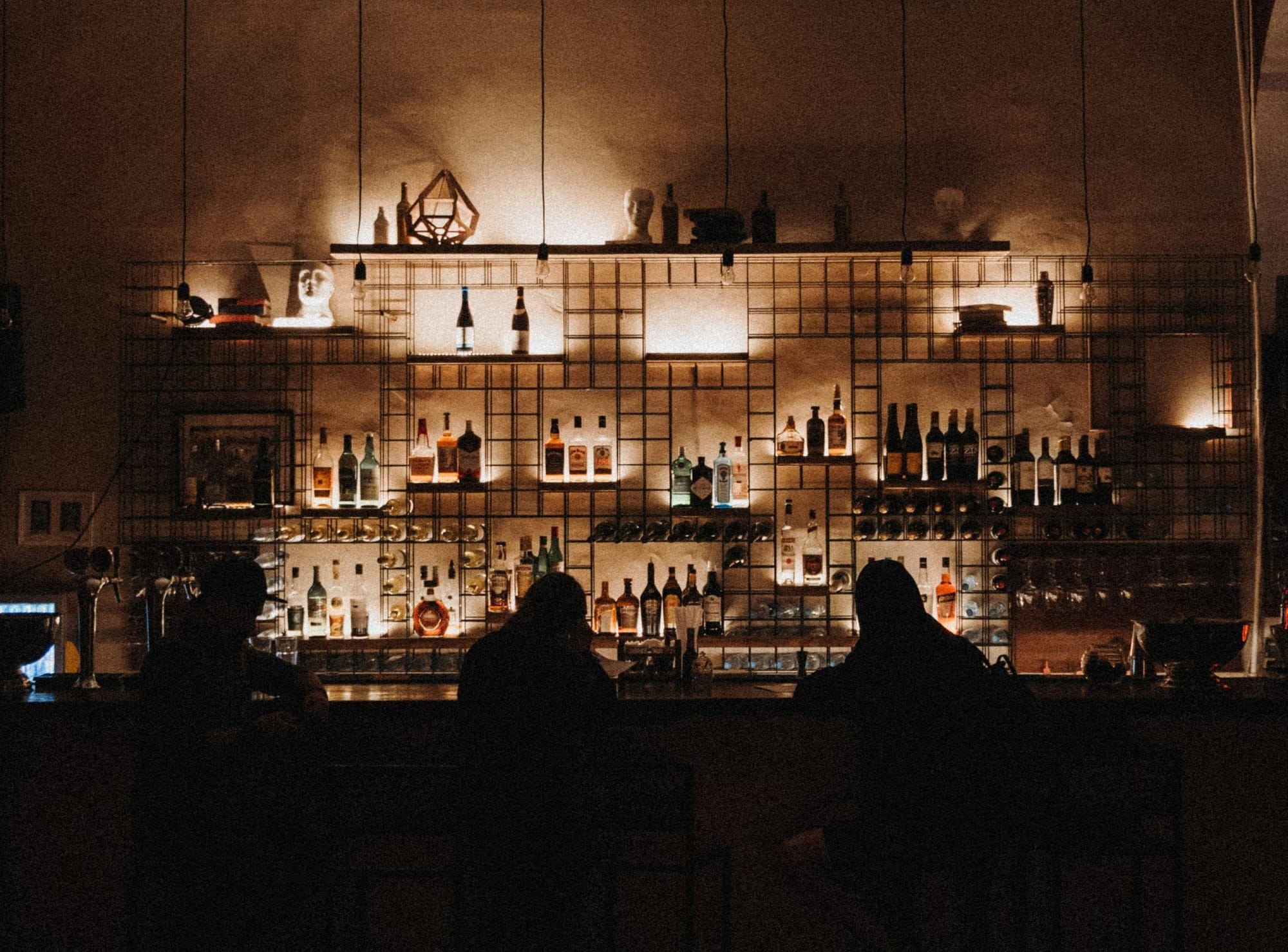 Patrons sit at a bar in moody lighting.