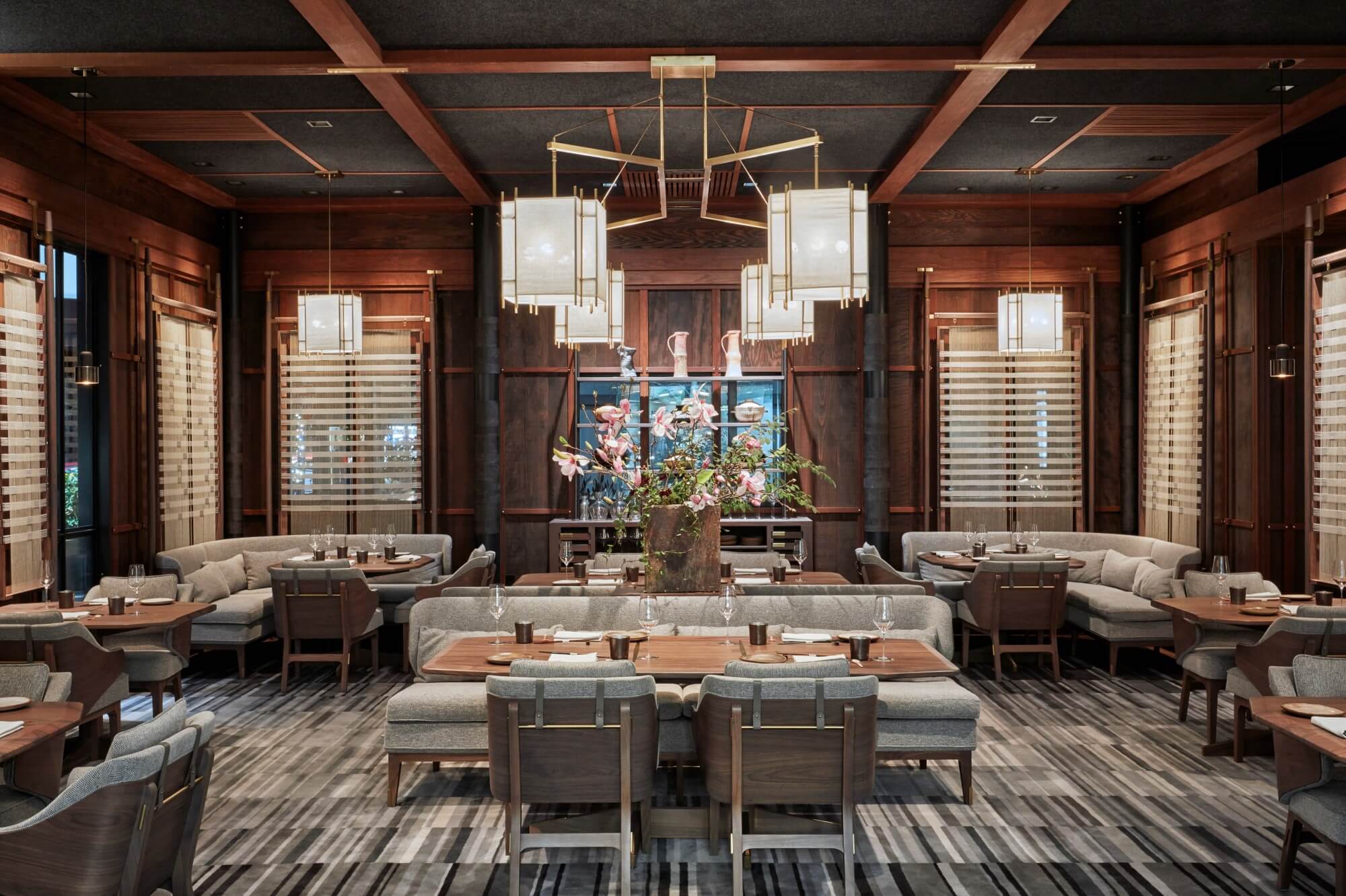 The dining room at SingleThread restaurant in Healdsburg, California, with warm wood-paneled walls, upholstered booths, set tables, and a large floral arrangement at center.