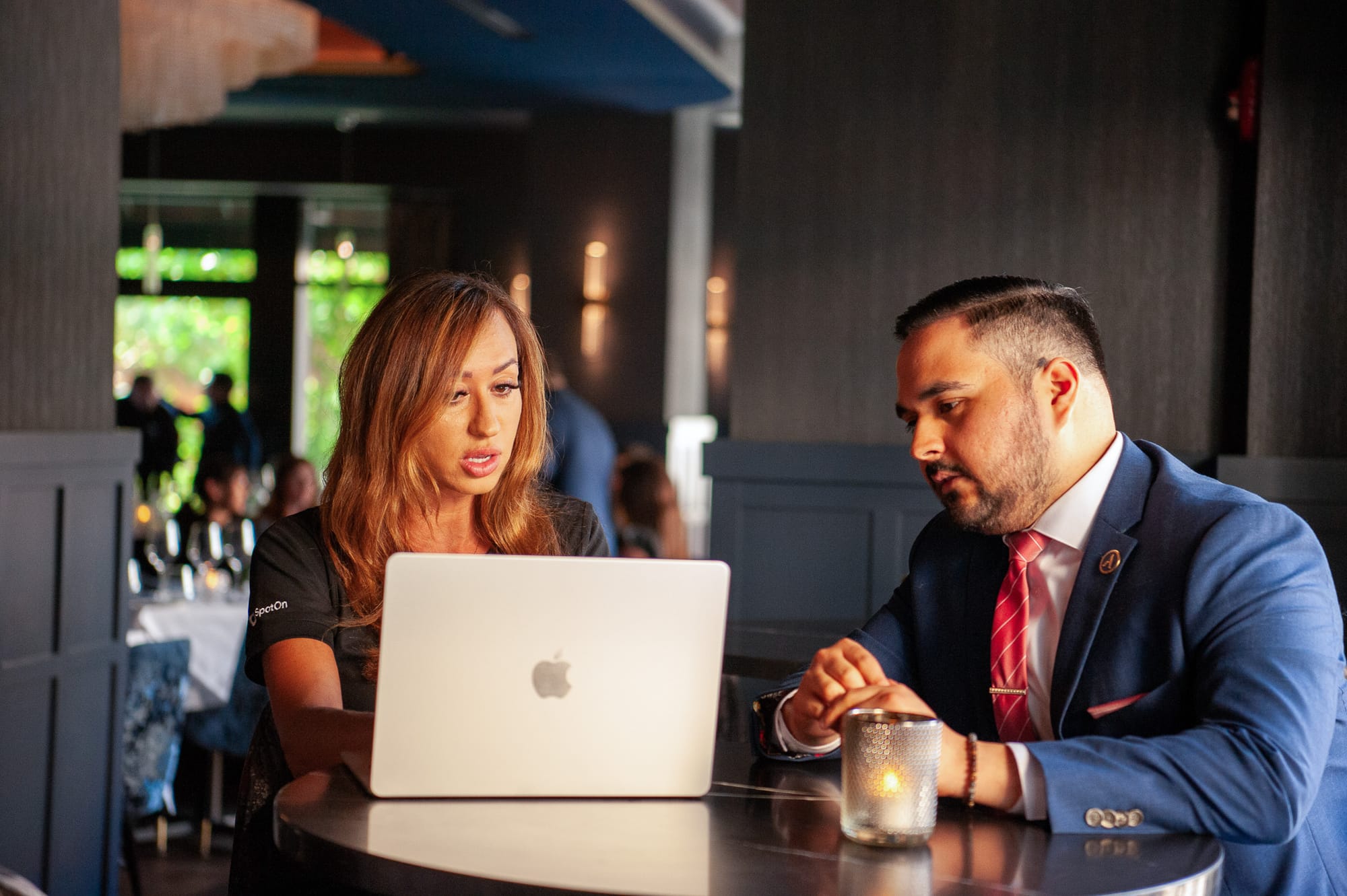 A SpotOn representative reviewing POS setup with a restaurant manager on a laptop inside a restaurant.