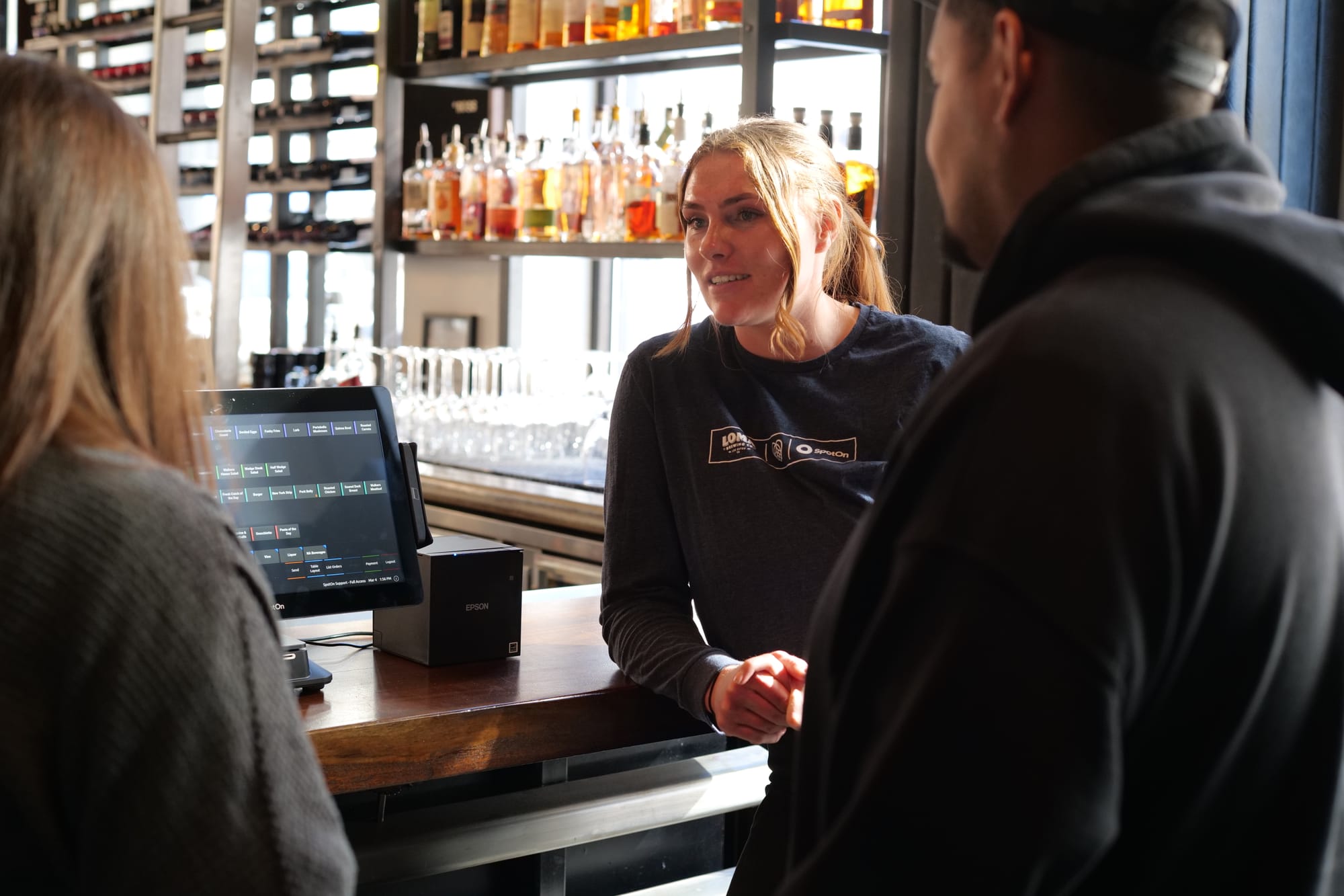 A SpotOn representative training restaurant staff on a point-of-sale system at a bar.